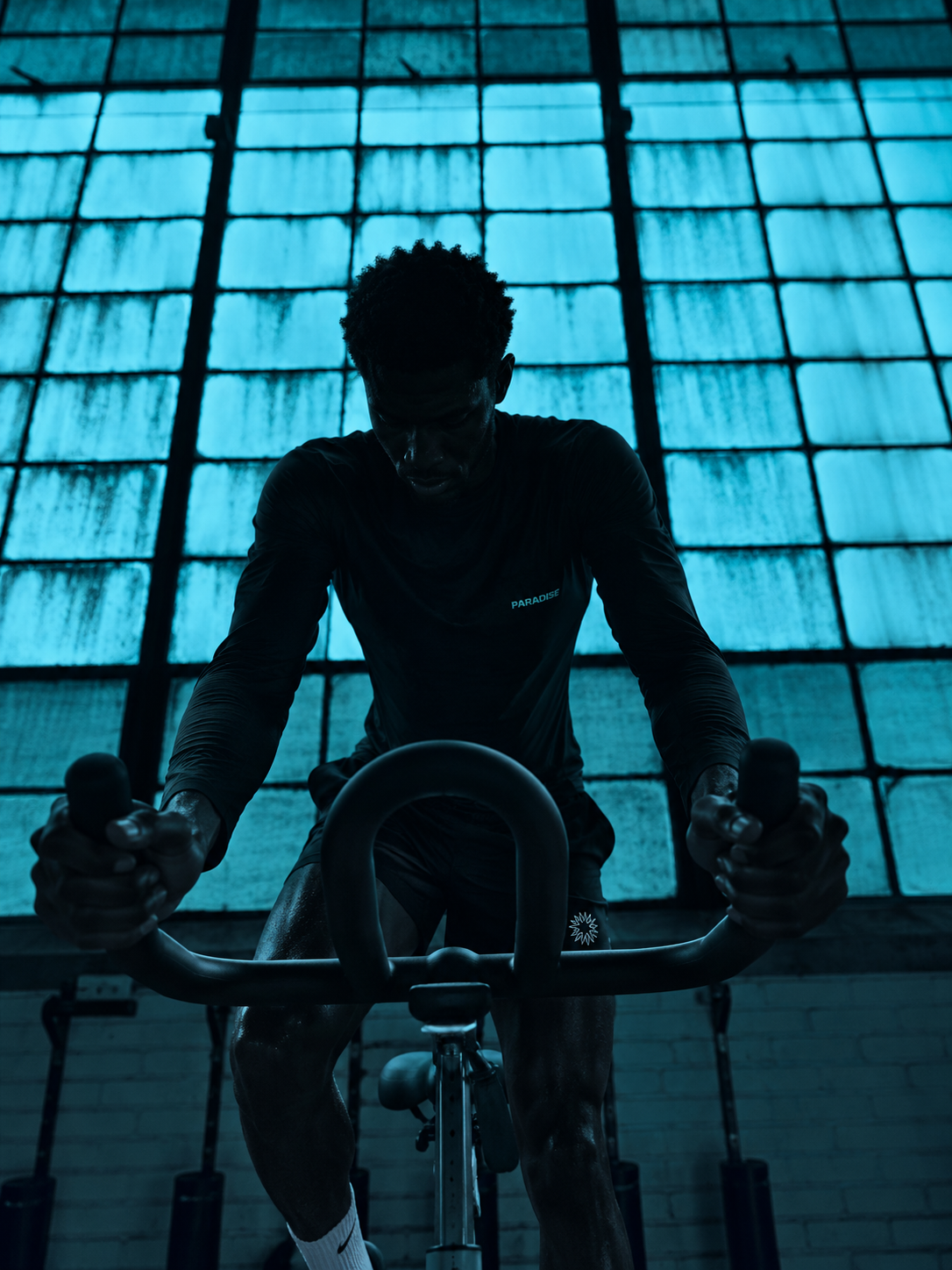 Athlete training on a stationary bike in Paradise Zero apparel, framed by blue-lit windows.