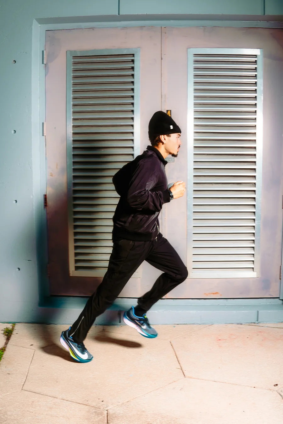 Runner in black Paradise Zero layers passing a pale Miami doorway.